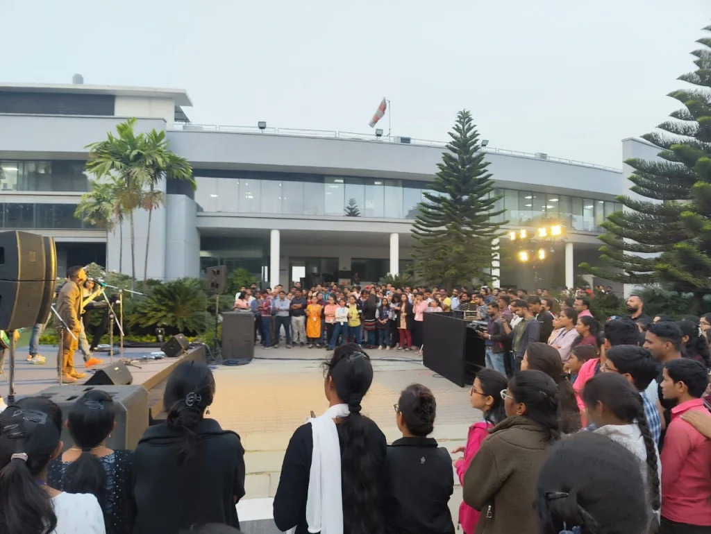 A live musical performance on an outdoor stage at a modern corporate campus with a large audience of employees.