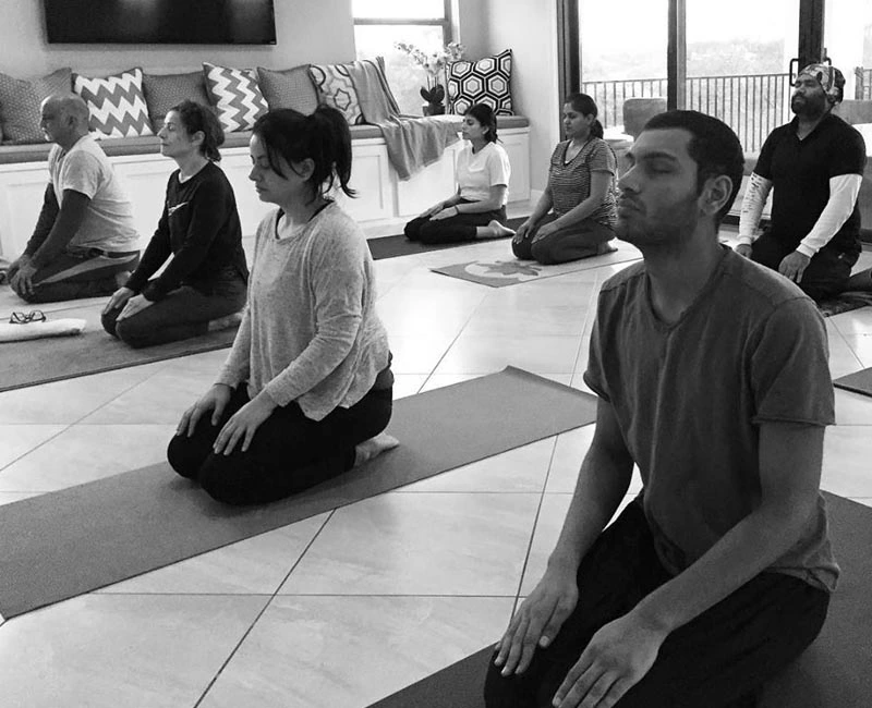A black and white photo of professionals sitting in a kneeling meditation pose on yoga mats during a corporate wellness retreat.