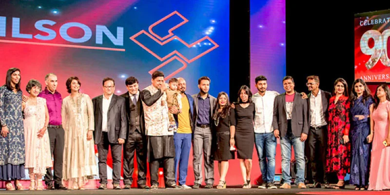 A group of diverse employees and their family members standing together on a stage celebrating a company's 90th anniversary.
