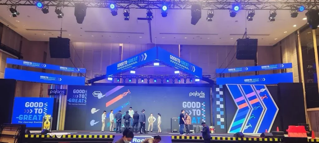A large corporate event stage for "Polaris 2024" with a racing theme, featuring "Good to Great" branding and blue LED geometric trusses.