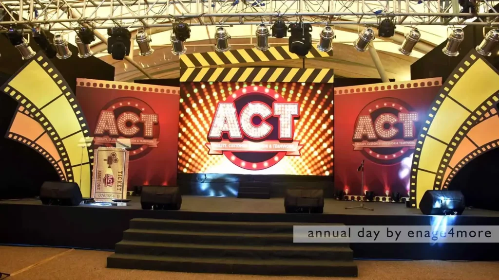A professional event stage with a "ACT" movie-themed backdrop, film reel decorations, and stage lighting.