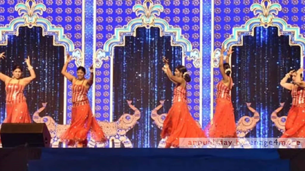 Five female dancers in red and gold outfits performing a synchronized routine on a blue-lit stage with ornate arch backdrops.