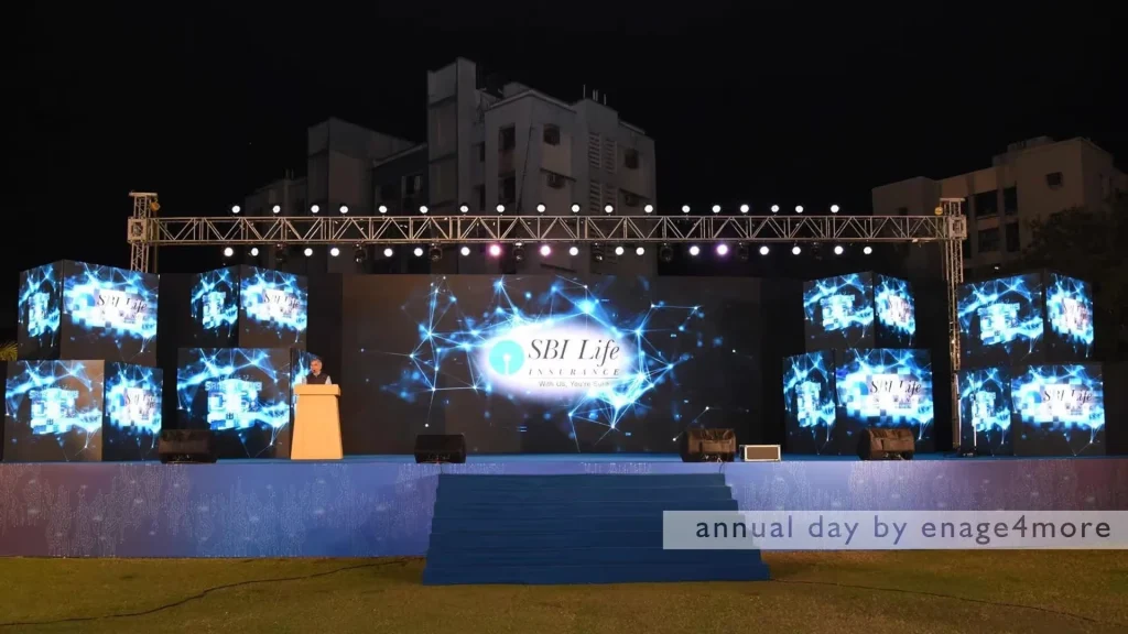 A grand outdoor stage at night for SBI Life Insurance with large LED screens displaying blue digital network patterns.