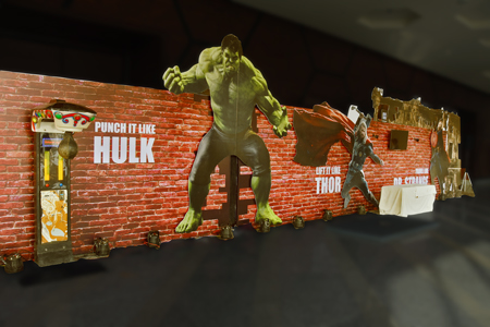A brick-wall themed interactive photo and activity zone for a corporate event featuring life-sized Avengers cutouts like Hulk and Thor with engagement challenges.