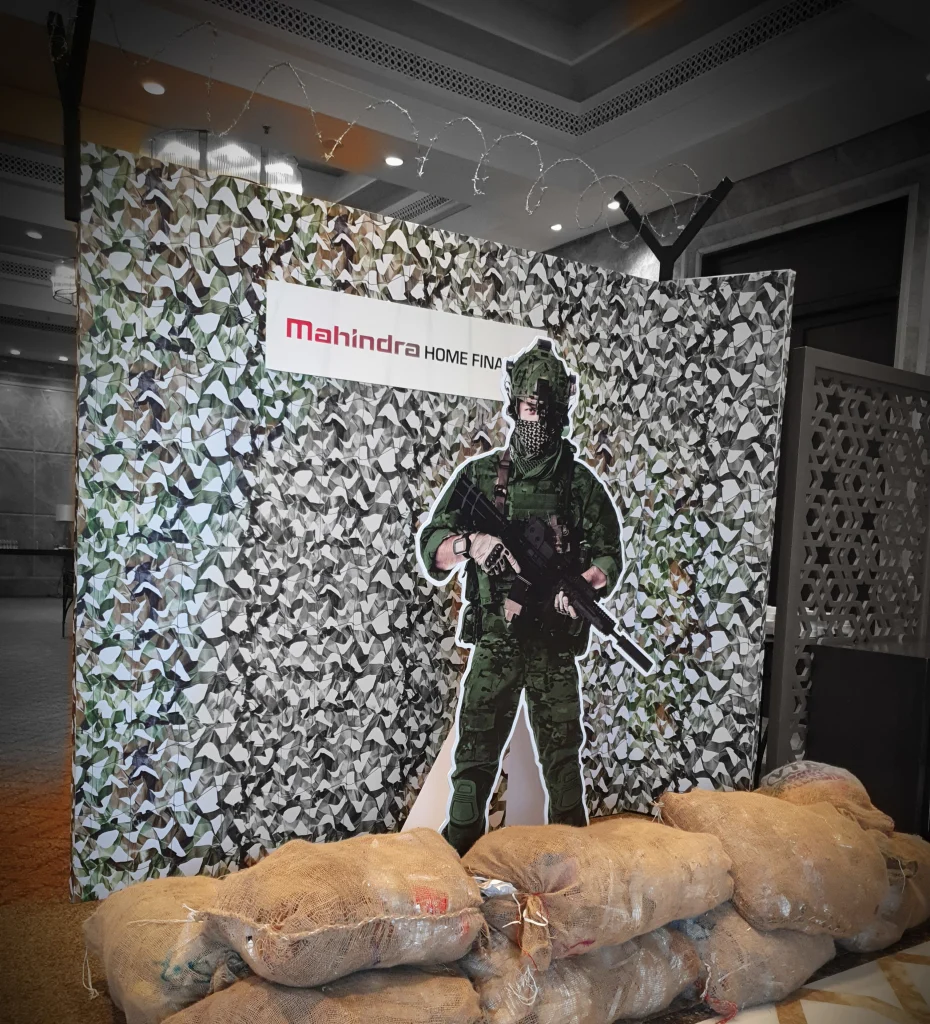 A military-themed photo booth for Mahindra Home Finance featuring a soldier cutout, camouflage backdrop, and sandbags.