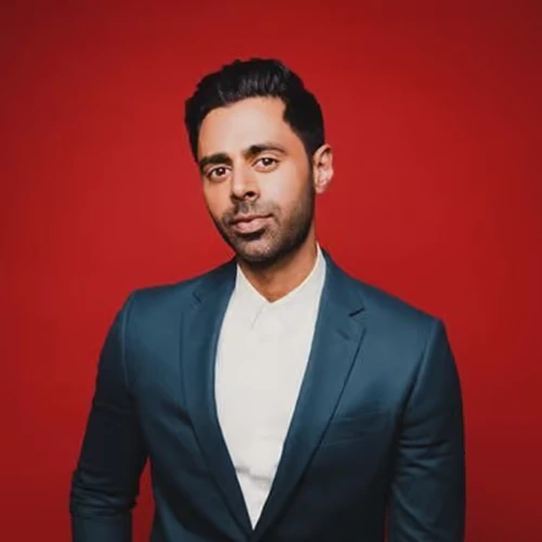 hasan-minhaj-comedian-political-satirist American comedian and political satirist Hasan Minhaj posing in a suit against a red background