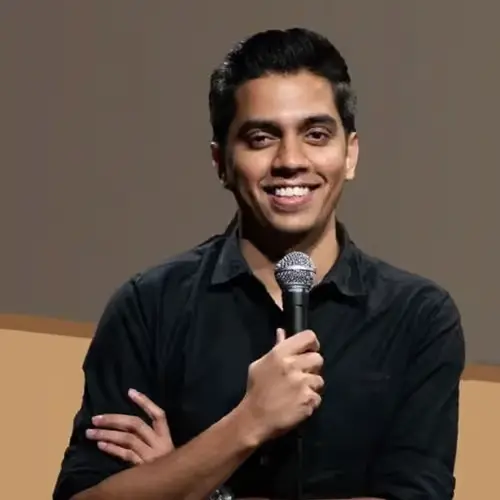 Comedian Shridhar Venkataramana smiling, arms crossed, holding a microphone, dressed in a black shirt