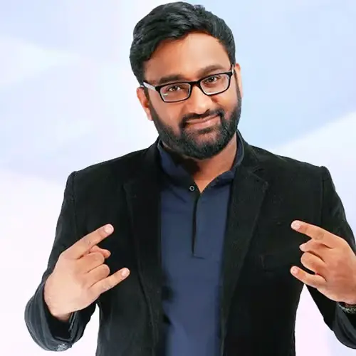 Comedian Vikash Paul smiling, wearing glasses and a blazer, making a rock-and-roll hand gesture