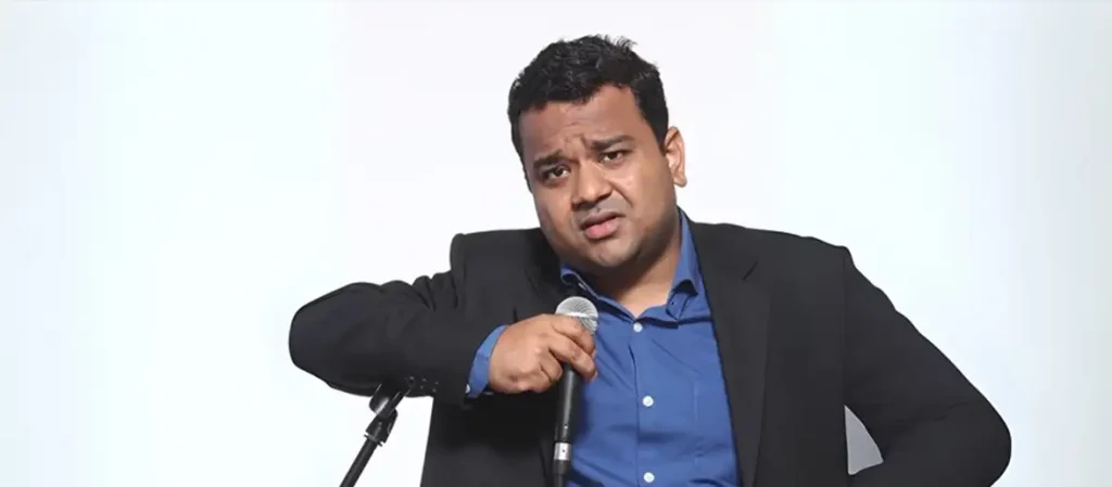 Kumar Varun, office comedy specialist, holding a microphone on stage and wearing a blue shirt with a black blazer