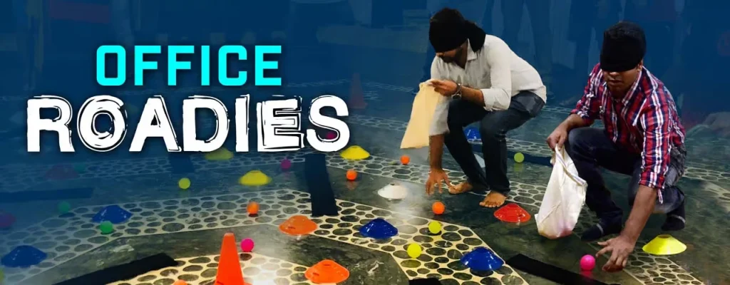 A group of young, diverse corporate employees in an Indian office setting, cheering and celebrating enthusiastically during a team-building game or competitive event.