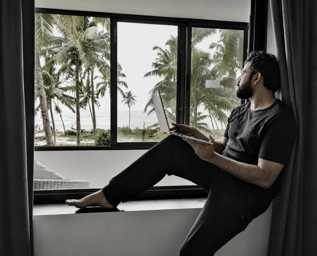 Cybersecurity specialist working on a laptop from a seaside window overlooking palm trees and the beach