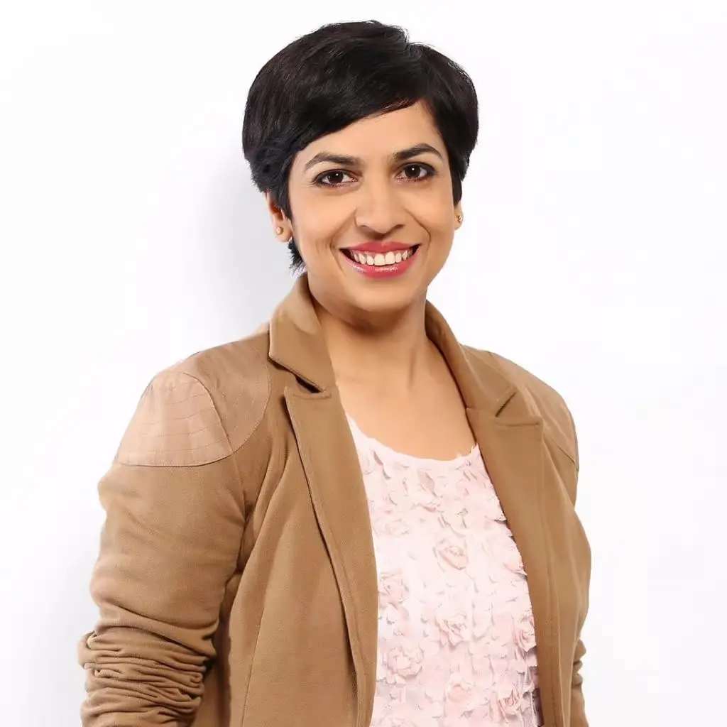 Major Vandana Sharma smiling, wearing a tan blazer over a textured pink top