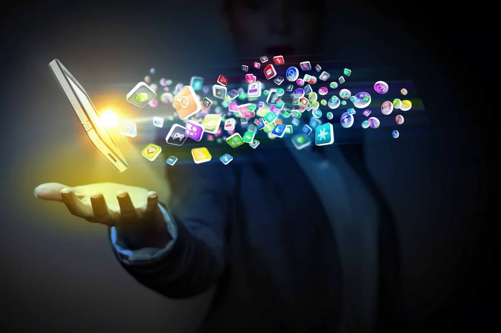 Mobile-Apps-Corporate-Engagement-Digital-Tools A close-up of a person holding a smartphone displaying various colorful mobile app icons, with a blurred office background, symbolizing digital connectivity and HR tech solutions.