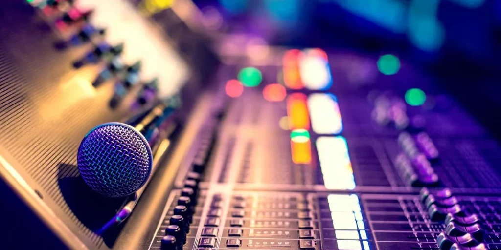 Corporate-Radio-Podcast-Employee-Engagement A professional silver microphone resting on a sophisticated sound mixing console with glowing purple and orange LED lights in a radio studio setting.