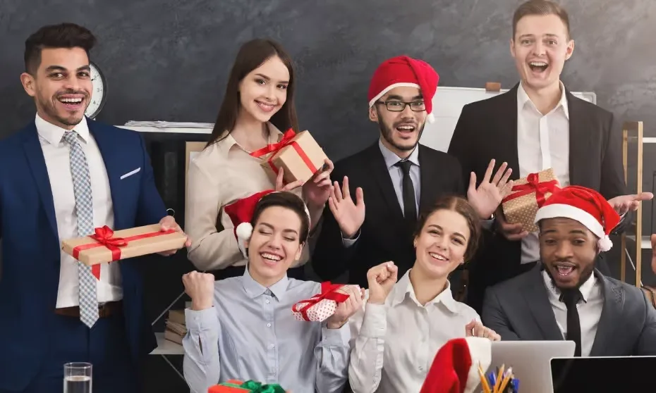 A group of seven happy corporate professionals in an office setting, wearing red Santa hats and holding wrapped gifts with red ribbons while celebrating cheerfully.