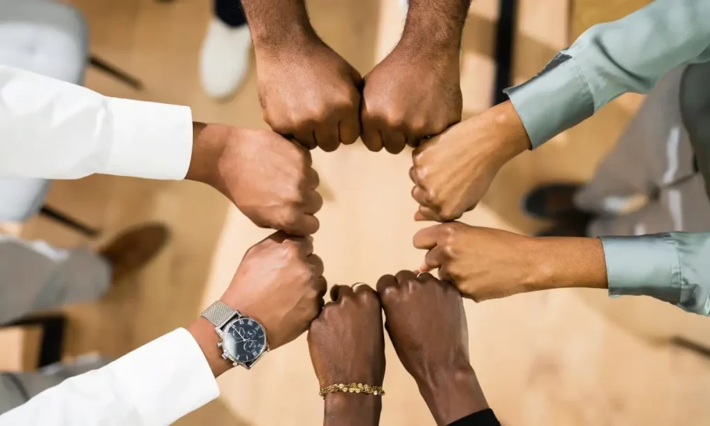 An overhead view of a diverse group of professionals standing in a circle, bringing their fists together in the center to signify unity and collaboration.