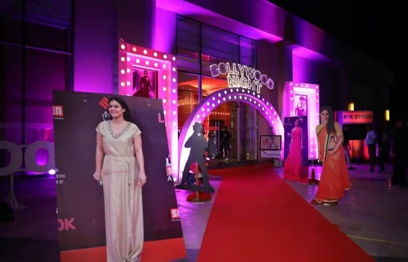 A vibrant purple-lit red carpet entrance for a corporate "Bollywood Night" event, featuring life-sized celebrity cutouts, a marquee archway, and a professional "Box Office" setup.
