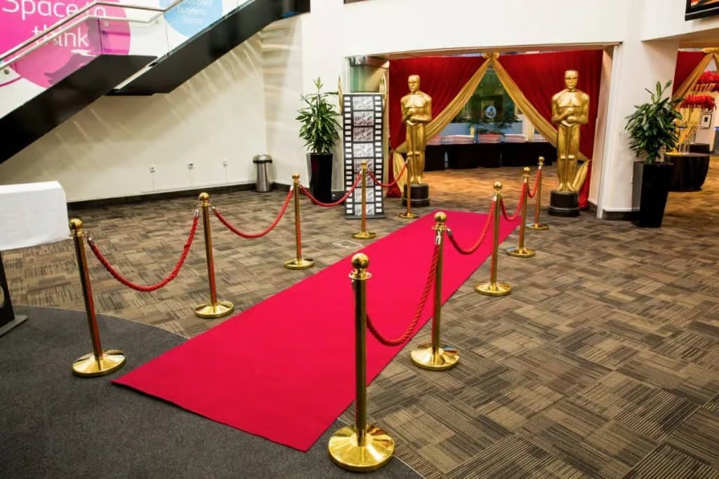 A glamorous red carpet entrance for a corporate "Oscar Night" event, featuring golden stanchions with red velvet ropes and a life-sized golden Oscar statue cutout under professional spotlights.