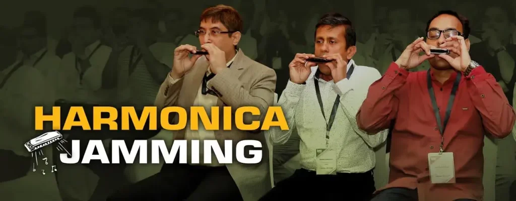 Three professional men sitting and playing harmonicas together during a corporate workshop, representing the "Kinship (K)" pillar of team engagement.