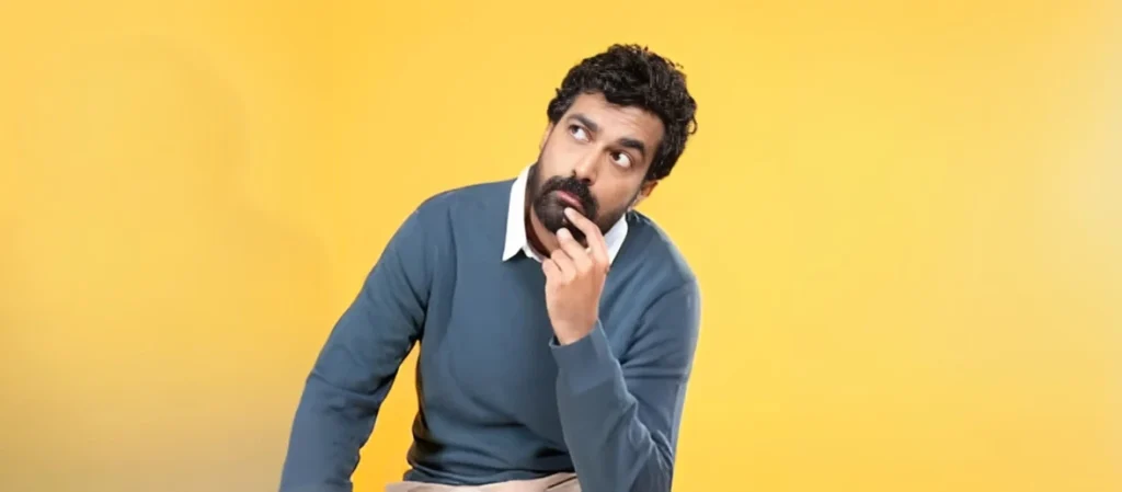 azeem-banatwalla-stand-up-comedian Indian stand-up comedian Azeem Banatwalla thinking with a hand to his chin against a yellow background