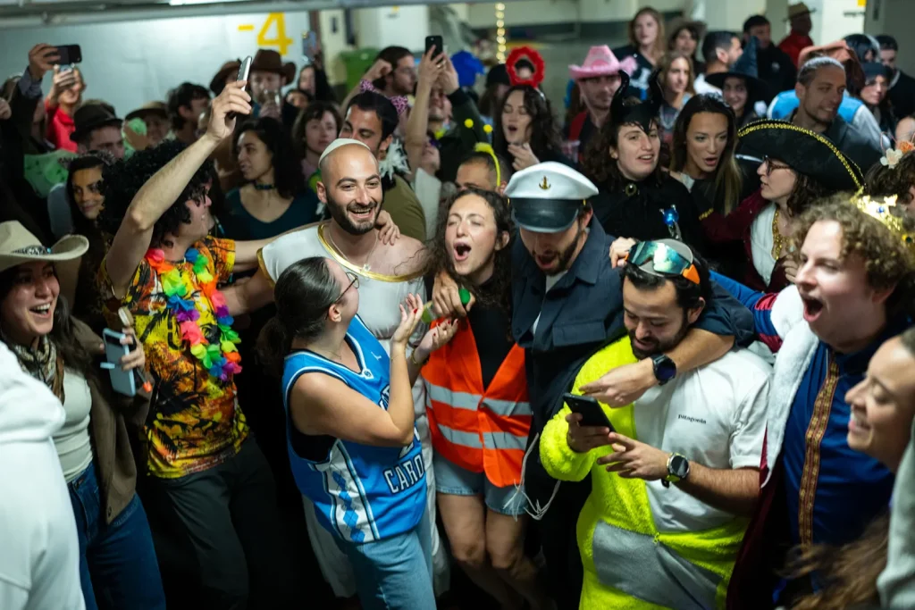 A vibrant group of people in colorful costumes singing and dancing together in an underground bunker in Israel during a period of conflict.