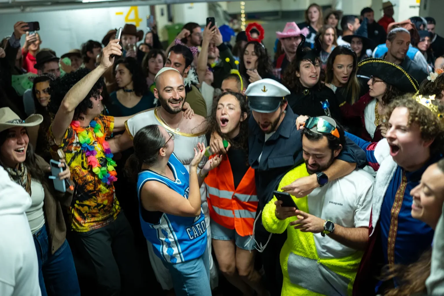 A vibrant group of people in colorful costumes singing and dancing together in an underground bunker in Israel during a period of conflict.