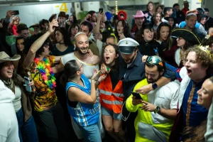 A vibrant group of people in colorful costumes singing and dancing together in an underground bunker in Israel during a period of conflict.