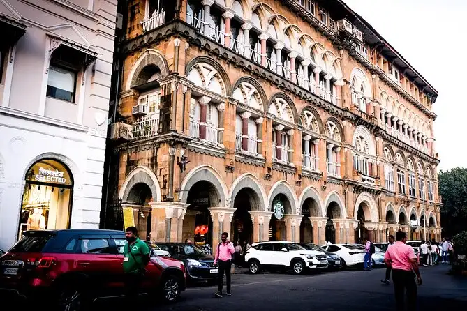 south-mumbai-heritage-walk-team-building The historic, ornate Gothic-style facade of a heritage building in South Mumbai, featuring multiple rows of arched windows and columns, with pedestrians and parked cars in the foreground.