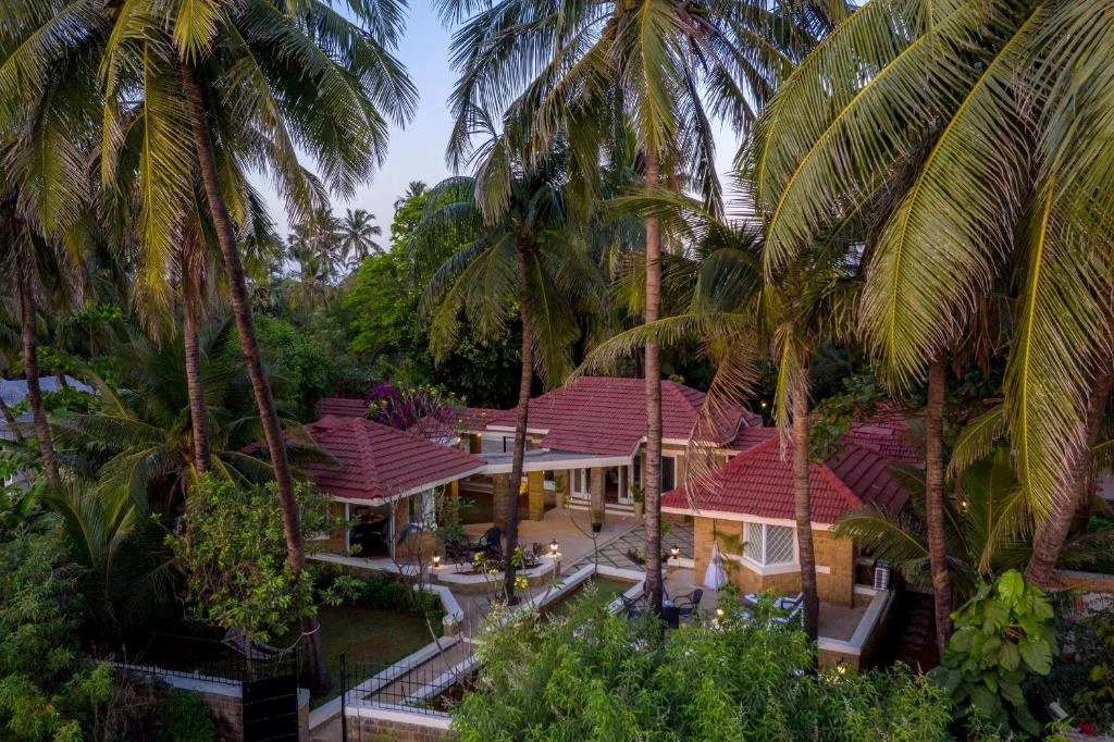 the-resort-madh-island-mumbai-urban-oasis-venue An aerial evening view of luxury red-tiled villas nestled among dense coconut palms at The Resort, Madh Island, showcasing a tranquil urban oasis.