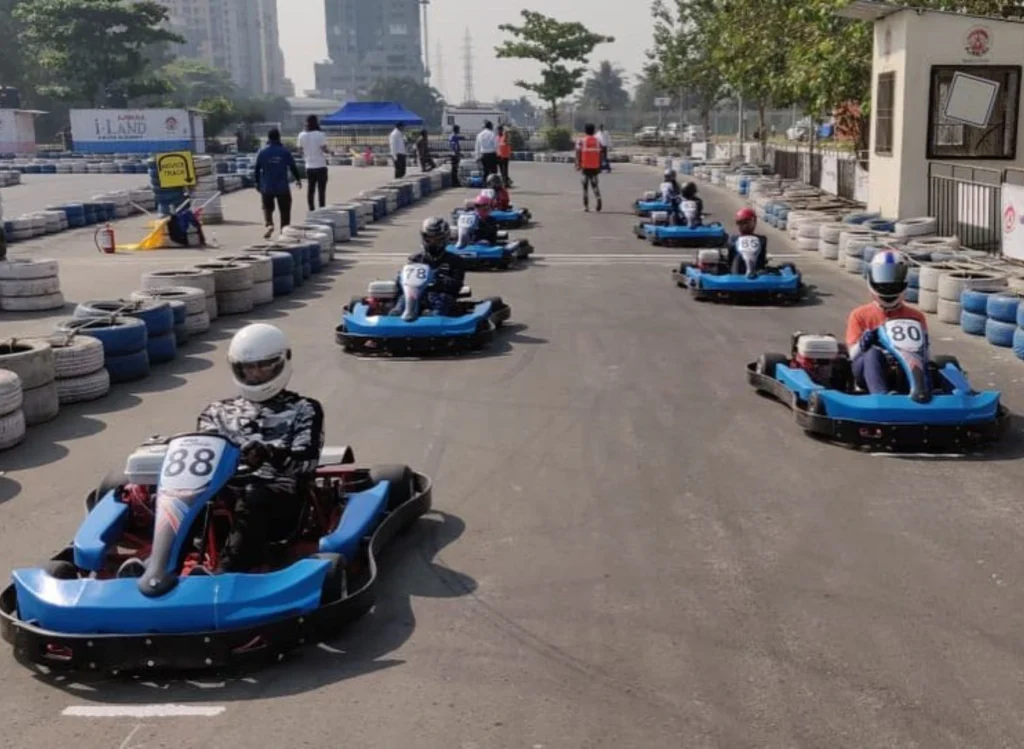 go-karting-mumbai-lower-parel-panvel-agility-circuit A lineup of blue and black go-karts with drivers in helmets positioned at the starting grid of a professional outdoor racing track in Mumbai.