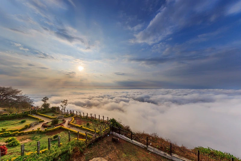 A breathtaking view of the sunrise above a blanket of clouds from the peak of Nandi Hills, a top destination for team outings near Bengaluru.