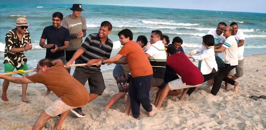 A corporate team engaged in a high-energy tug-of-war activity on Alibaug beach during a strategy retreat.