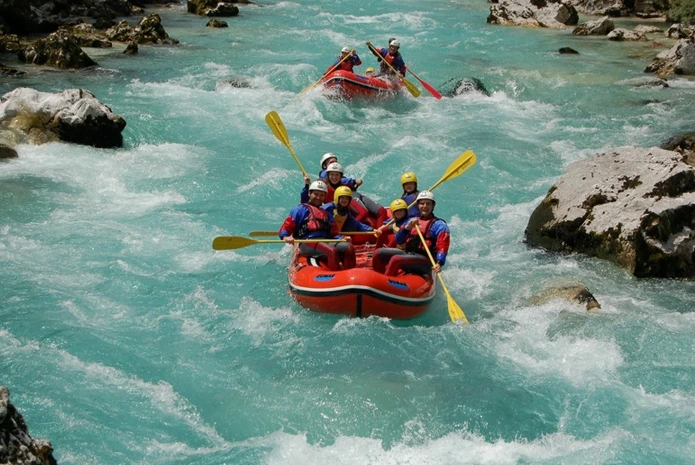 A high-energy action shot of two red inflatable rafts navigating turquoise white-water rapids in Rishikesh, with teams of corporate professionals in helmets and life jackets paddling in synchronization.