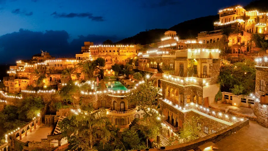 A dramatic night photograph of the historic Neemrana Fort-Palace near Delhi, fully illuminated with warm lights, built into the side of an Aravali hill—a top luxury team-building location.