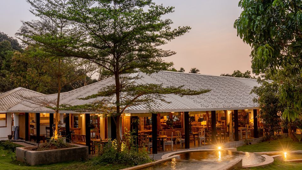 karjat-riverside-reset-oleander-farms-team-building A warm night exterior shot of the Saltt restaurant at Oleander Farms in Karjat, featuring a lit-up open-air structure surrounded by lush trees and a small pond.