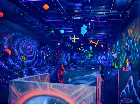 Interior view of a neon-lit laser tag arena in Delhi featuring cosmic wall murals, glowing planets, and tactical partitions—an ideal venue for high-energy corporate team building.