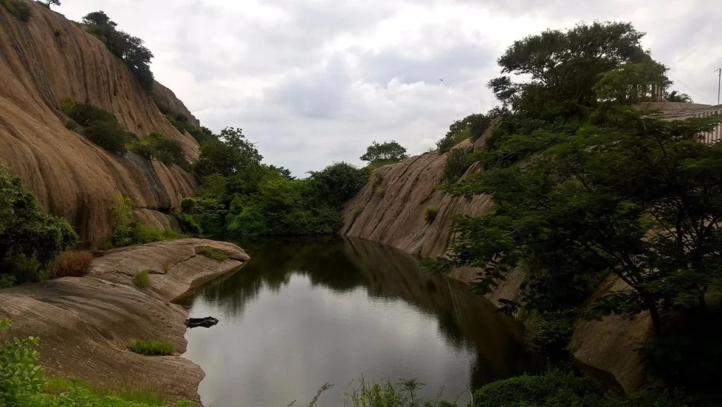 A serene natural pond surrounded by massive granite hills in Ramanagara, a popular spot for corporate team building and rock climbing near Bangalore.