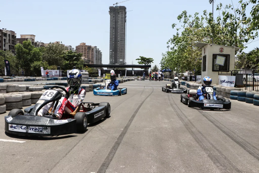 ajmera-indikarting-mumbai A high-angle view of the Ajmera IndiKarting track in Wadala, Mumbai, featuring a wide tar race track, bright floodlights, and parked go-karts ready for a corporate race.