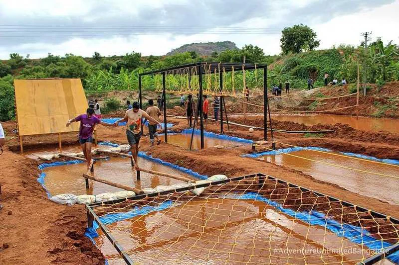 Employees participating in a muddy obstacle course and balance challenge at Kanakapura Nature Adventure Camp near Bengaluru.