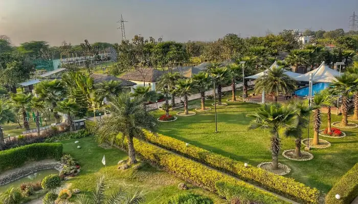 Overhead view of the lush green lawns, palm trees, and rural-themed architecture at Rurban Village near the Delhi-UP border—a dedicated venue for grounding corporate team building activities.