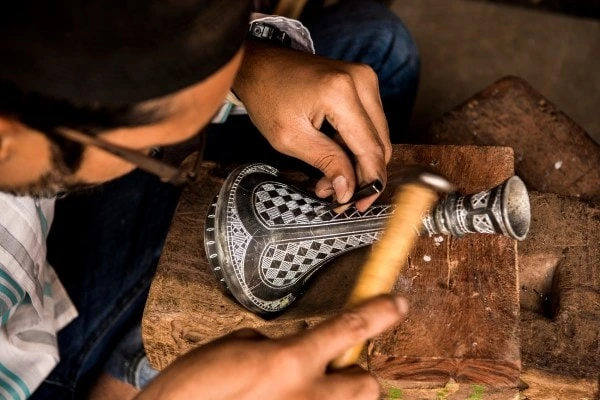 An artisan carefully hand-chiseling intricate silver patterns into black Bidriware metal in a traditional Hyderabad workshop