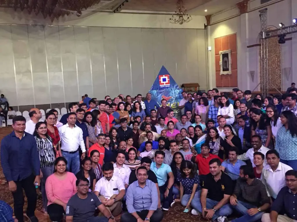 A large corporate team from HDFC Bank posing together after completing a "Build a Pyramid" engagement activity in a ballroom.
