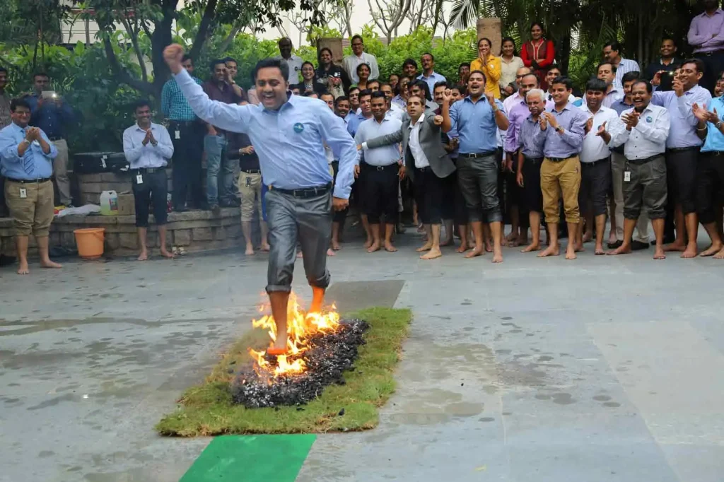 fearless-josh-fire-walk-peak-performance-mumbai A corporate professional performing a Fire Walk on burning coals while a large group of colleagues cheers in the background.