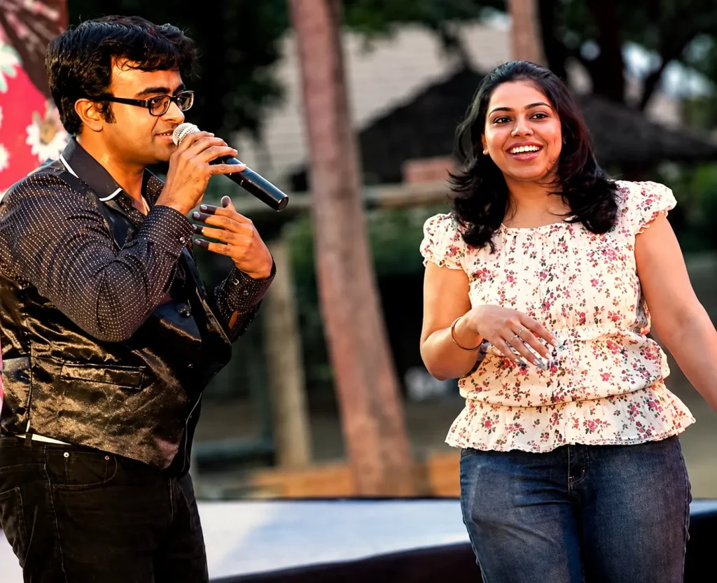 A man hosting and a woman participating in an energetic corporate Antakshari session held in an office environment.