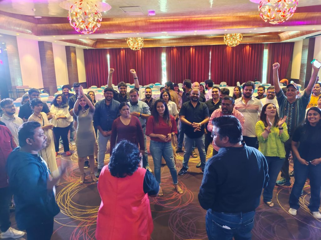 A large group of employees laughing and participating in a high-energy corporate engagement session in a hotel hall.