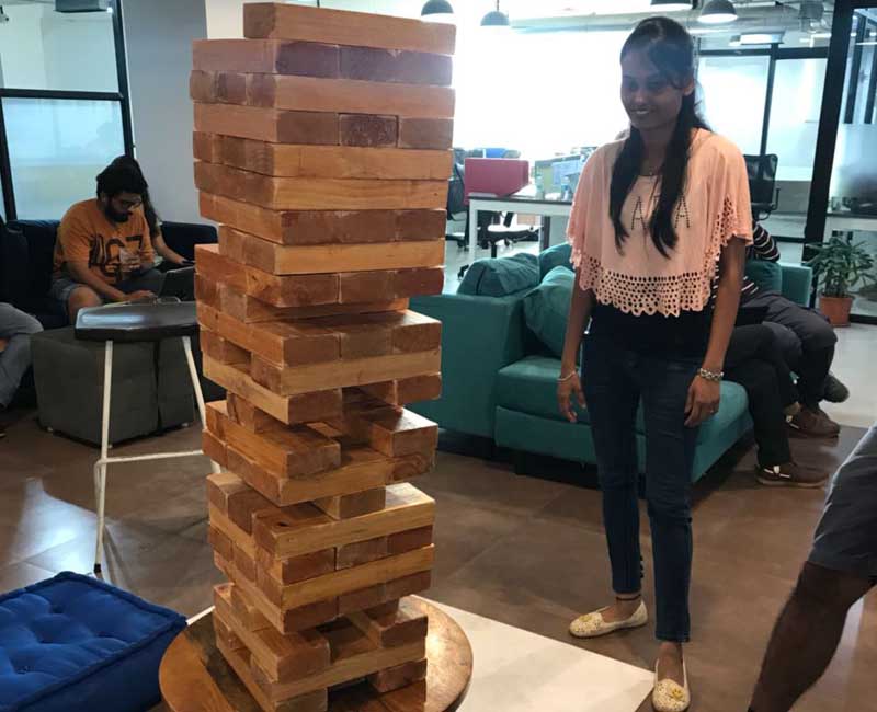 A woman standing next to a giant wooden Jenga tower during a corporate office engagement session.